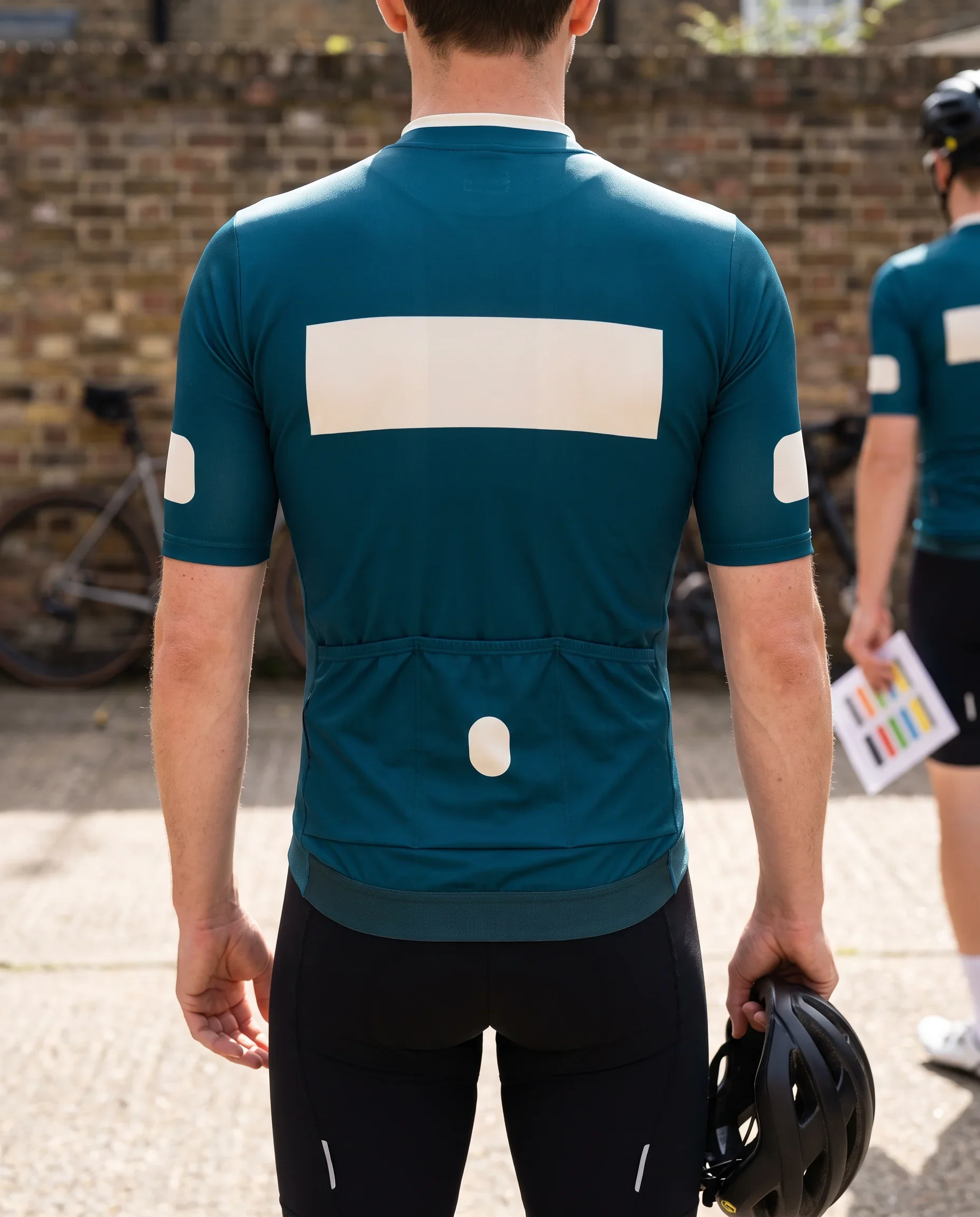 A club rider seen from behind in a teal team jersey, the sponsor zones on collar, upper back, sleeves, pocket and hem shown as plain colour blocks